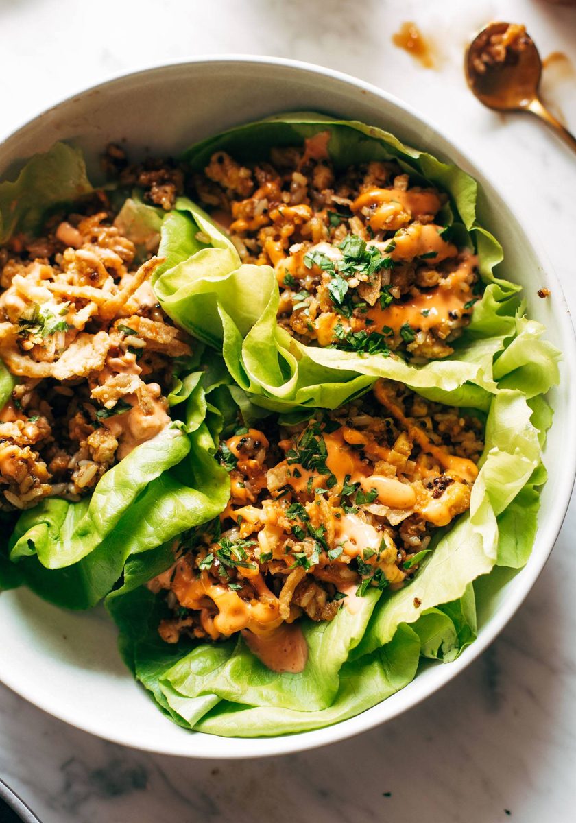 Lettuce wraps on a plate. The wraps are filled with tofu and brown rice and have sauce drizzled on top.