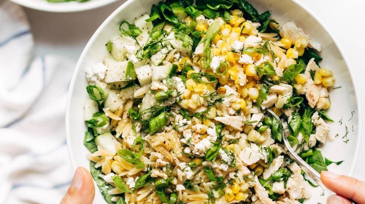 Hand holding Orzo Summer Salad in a bowl with fork.