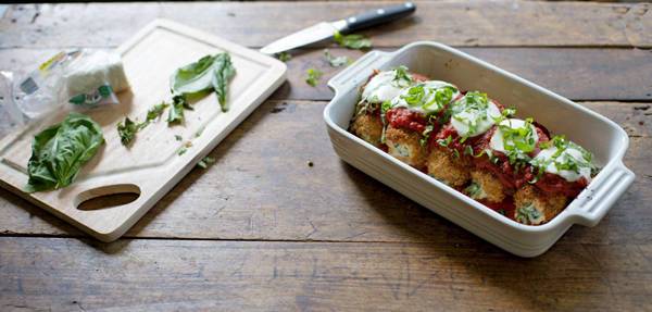 Basil on cutting board next to chicken rolls in a white baking dish.