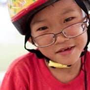 A young boy with glasses and a bike helmet on.
