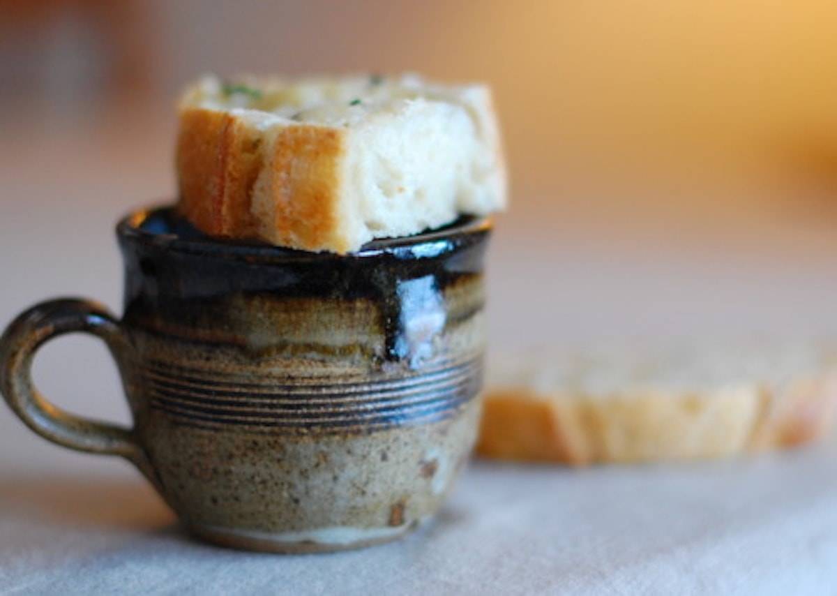 Bread on top of a clay mug containing soup.