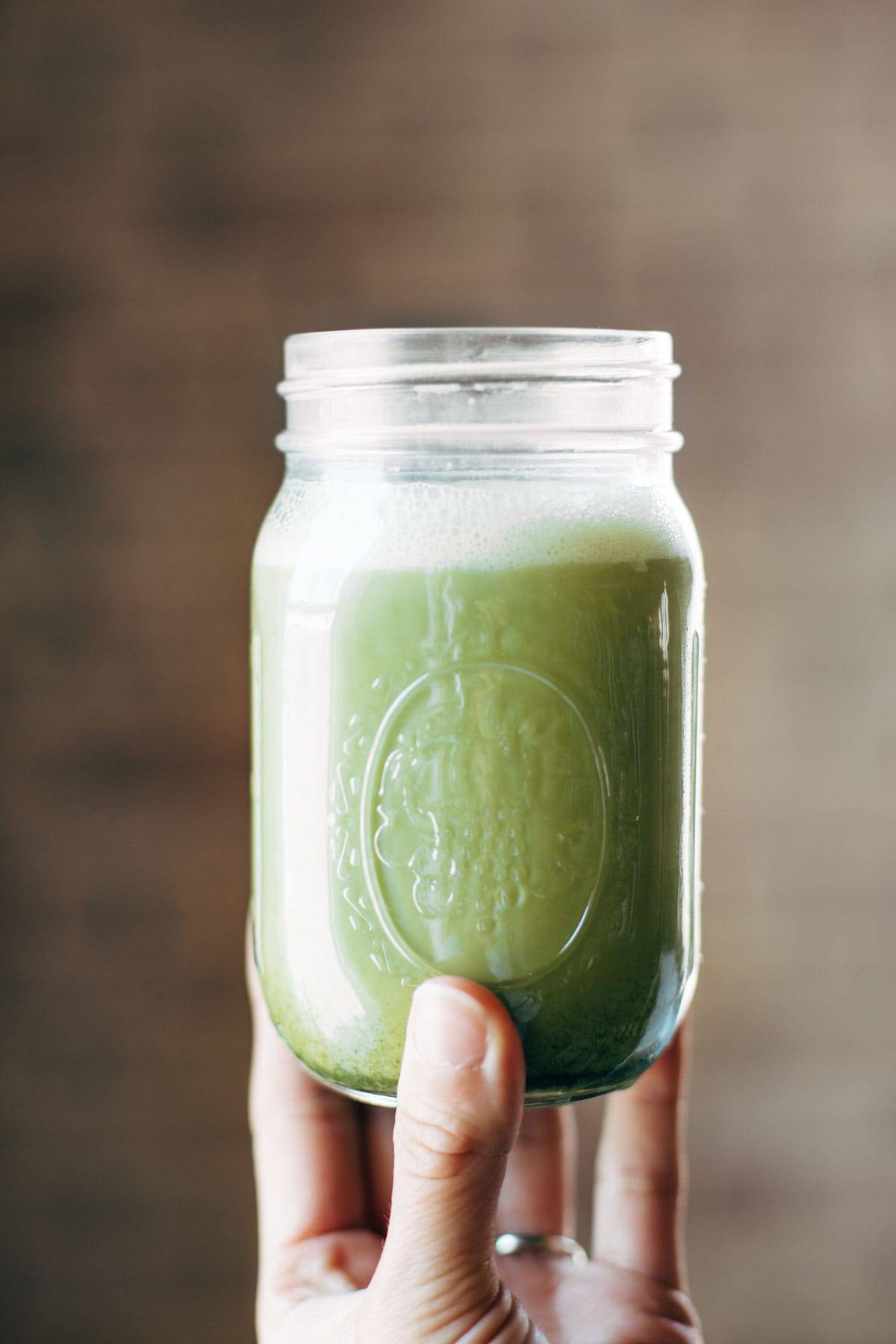 Iced Matcha Green Tea Latte shaken in a jar with a white hand holding it up.
